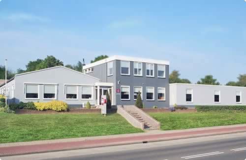 Graues Firmengebäude von THN an der Hendrink ter Kuilestraat mit roten Akzenten und Parkplätzen entlang der Straße
