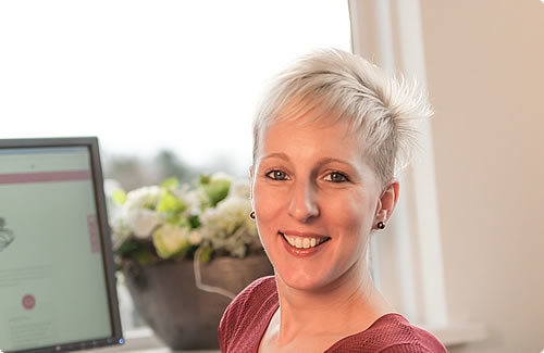 THN customer service representative with short blonde hair and a smile behind a desk with a screen