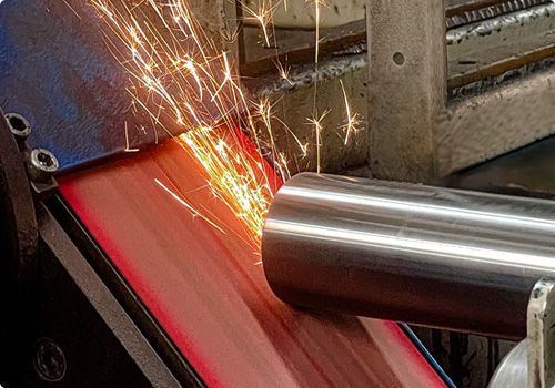 Assenbewerking op bandslijpmachine, vonken zichtbaar tijdens verspanen