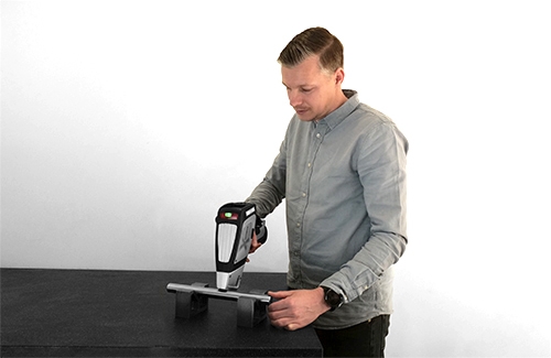 Man scant metalen as met XRF-scanner op zwarte tafel