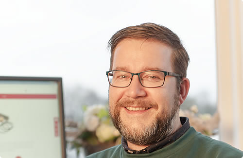 Lachende klantenservicemedewerker met bril bij THN achter bureau met beeldscherm