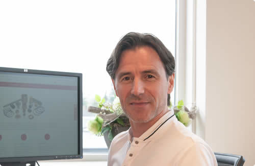 THN-medewerker met donker haar en witte polo aan bureau met monitor