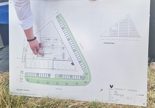 Vinger wijst naar bouwtekening van THN-terrein op gras